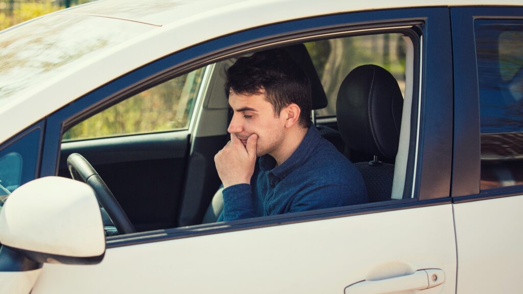 Ein nachdenklicher junger Fahrer, der seine Hand unter das Kinn legt und nervös in seinem Auto wartet.