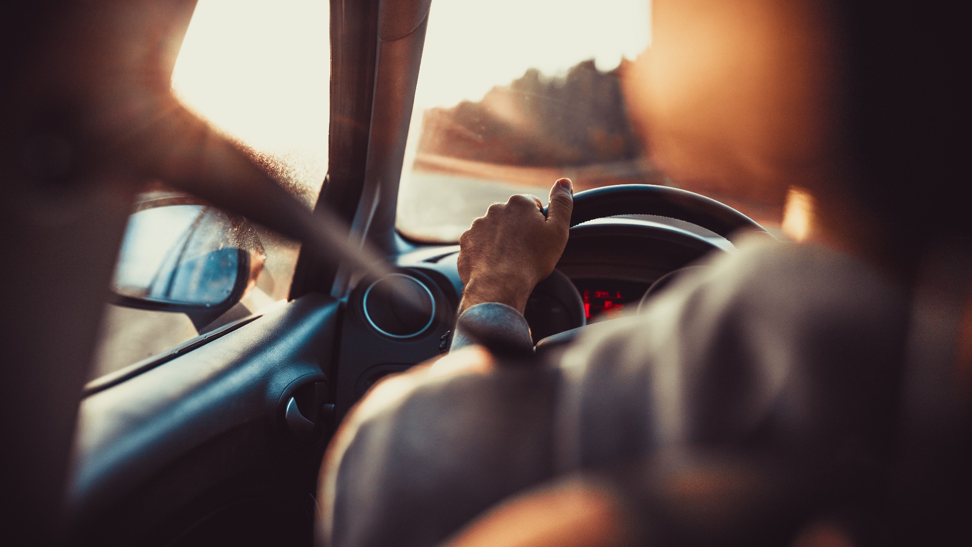 Mann fährt Auto, Hand am Lenkrad, schaut auf die Straße vor sich.