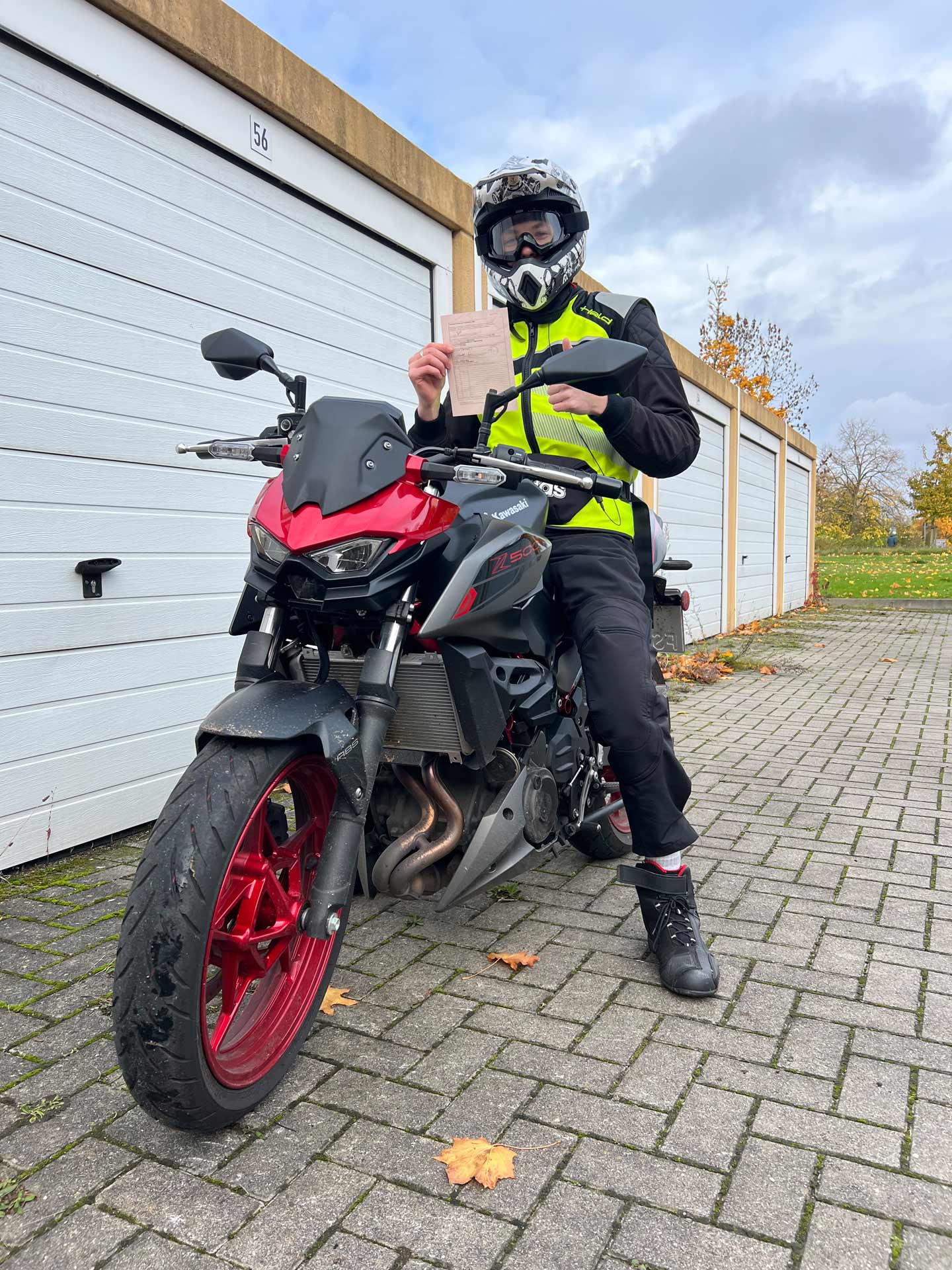 Eine Person mit Motorradhelm und Warnweste sitzt lächelnd auf einem roten Motorrad und hält ein Papier in der Hand